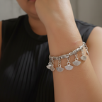 Woman wearing a silver bangle with charms, looking thoughtful.