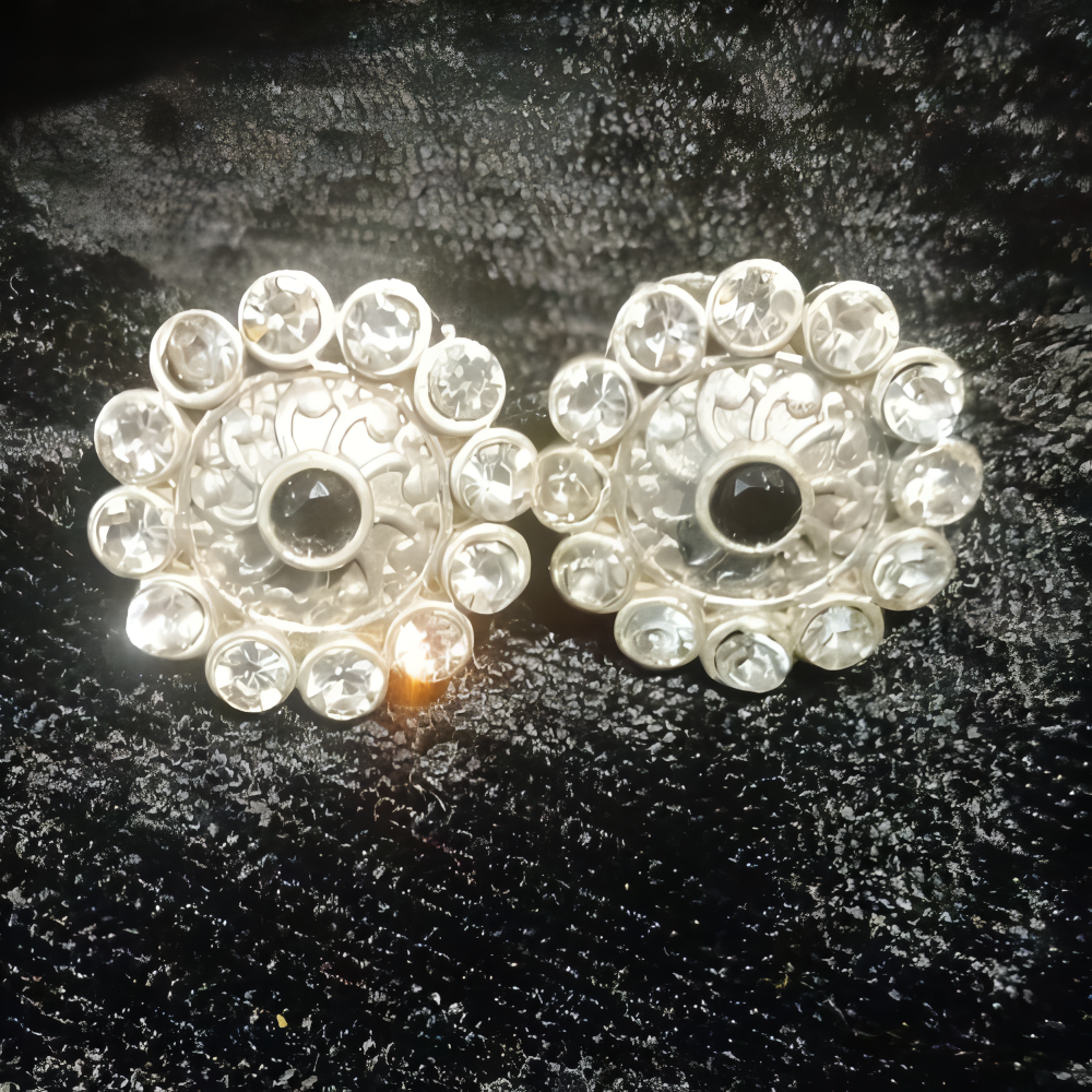 Pair of silver ornate earrings with black kundan stone at the centre & clear kundan stones all around.