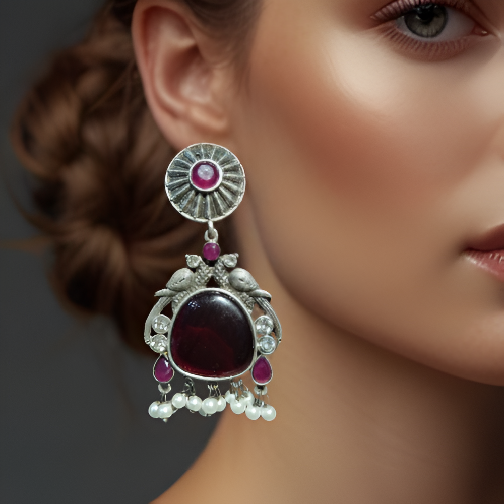 Close-up of a model ornate earring with a dark gemstone and pink stones on a blurred background