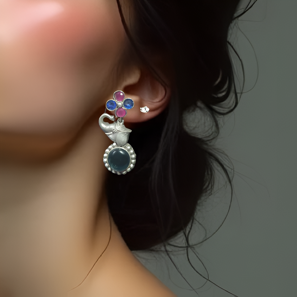 Close-up of a person wearing a silver earring with elephant inspired colorful stones.