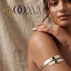 A woman wearing a wide silver cuff bracelet with two small black oval stones on her upper arm, with matching silver rings on her fingers. The brand logo 'SOOMA' is visible in the top left corner against a textured beige backdrop.