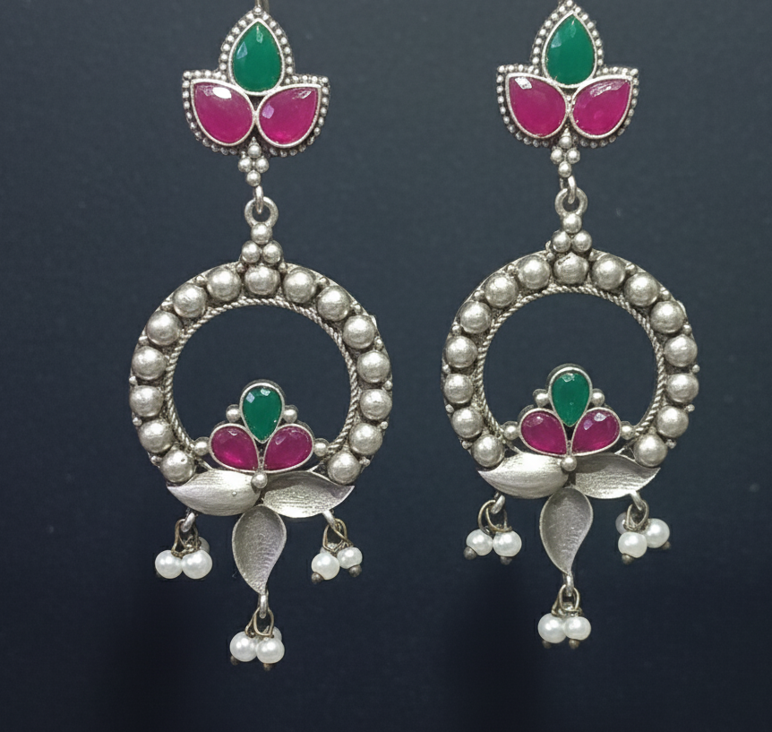 Pair of silver oxidised earrings with green and pink stones on a wooden background